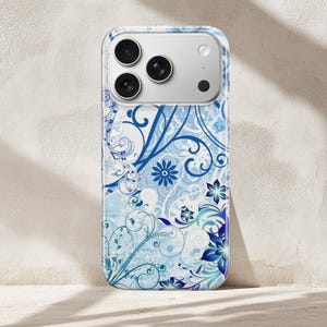 May include: A phone case with a floral design in shades of blue and white. The case features a repeating pattern of stylized flowers, swirls, and leaves. The phone case has a clear border and a camera cutout.