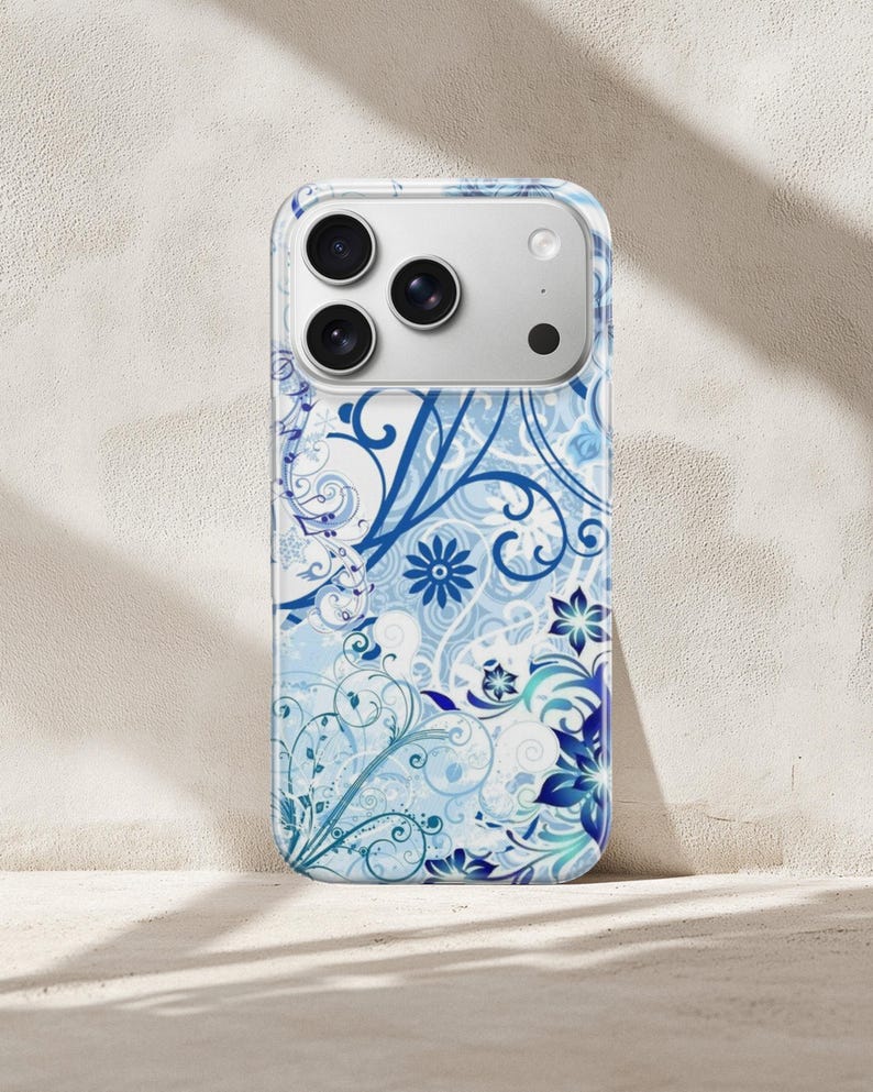 May include: A phone case with a floral design in shades of blue and white. The case features a repeating pattern of stylized flowers, swirls, and leaves. The phone case has a clear border and a camera cutout.
