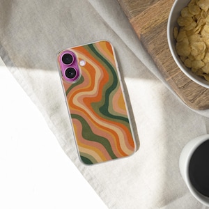 Pode incluir: Uma capa de smartphone com um padr&atilde;o ondulado colorido em tons de laranja, verde e bege. A capa est&aacute; sobre uma superf&iacute;cie clara, perto de uma tigela de cereais e uma x&iacute;cara de caf&eacute;.