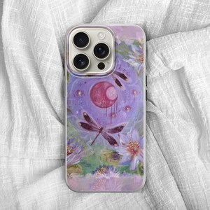 May include: A phone case featuring a watercolor design with a dragonfly, flowers, and a celestial motif. The case has a purple and pink color scheme with a glossy finish. The design includes a large, stylized dragonfly.