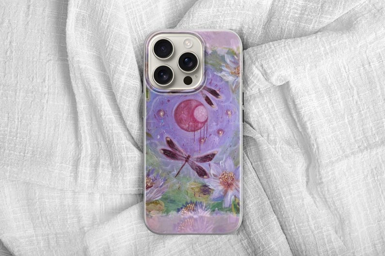 May include: A phone case featuring a watercolor design with a dragonfly, flowers, and a celestial motif. The case has a purple and pink color scheme with a glossy finish. The design includes a large, stylized dragonfly.