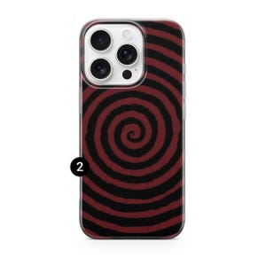 May include: A phone case with a red and black spiral design. The case has a clear border and a camera cutout. The spiral pattern covers the back of the case, creating a bold and eye-catching look. The case is designed to fit a smartphone.