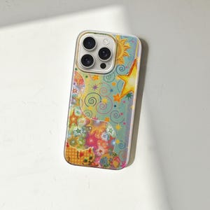 May include: A colorful phone case featuring a whimsical design with a sun, stars, and swirling patterns. The case has a clear border and a vibrant, artistic aesthetic. The design incorporates shades of blue, yellow, orange, and pink.