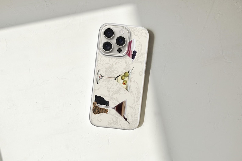 Puede incluir: Funda de tel&eacute;fono con un estampado floral blanco e ilustraciones de copas de martini. Las copas de martini contienen aceitunas, bayas y otras guarniciones. La funda tiene un protector de lente de c&aacute;mara transparente.