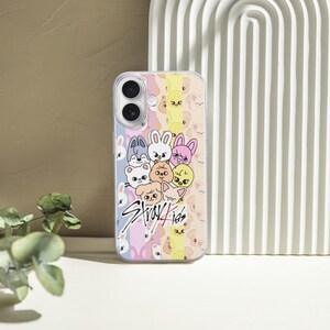 May include: A clear phone case featuring a colorful design with cartoon animal characters and the text "Stray Kids". The case has a pastel rainbow background and is set against a neutral backdrop.