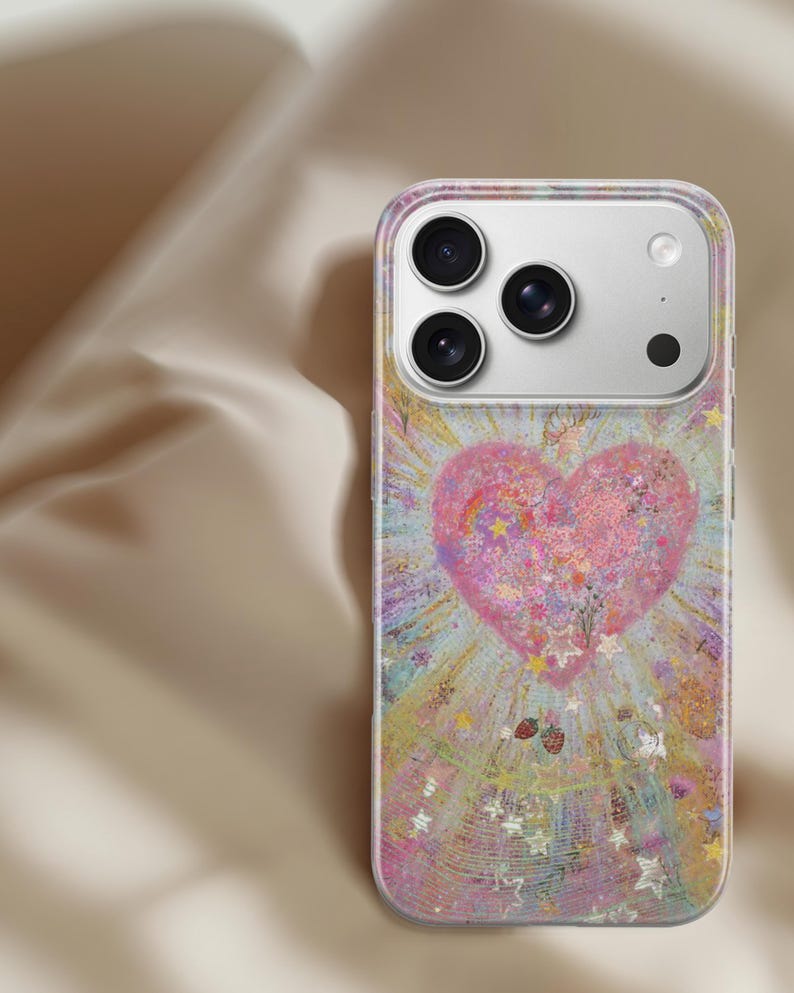 May include: A clear phone case featuring a colorful design with a large pink heart at the center. The heart is surrounded by a burst of light and stars, with small strawberries and glitter accents. The case has a clear border and covers the phone's back.