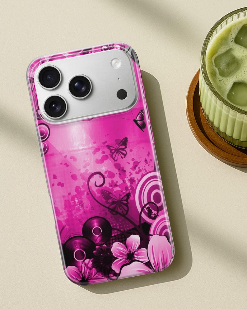 May include: A pink phone case with a butterfly and floral design. The case features a clear border and a vibrant pink background with abstract shapes, butterflies, and flowers. The phone's camera lenses are visible at the top.