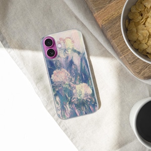 May include: A smartphone case with a floral design in shades of pink, purple, and blue. The case is on a light-colored surface, next to a bowl of cereal and a cup of coffee. The phone case has a pink camera module.