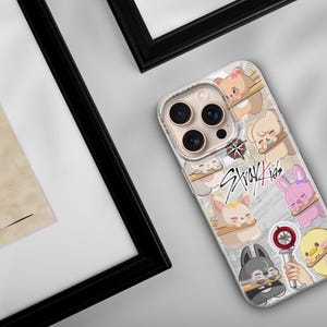 May include: A phone case with a design featuring cartoon animals and the text "Stray Kids". The case has a clear background with various cartoon characters, including bears, bunnies, and a wolf. The case is on a white surface.
