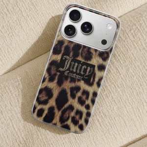 May include: A clear phone case with a leopard print design. The case features the text "Juicy Couture" in a black rectangle with a rhinestone effect. The phone case is on a beige surface.