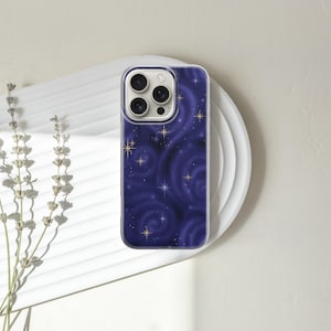 May include: A smartphone case with a dark blue, swirling galaxy design, featuring gold stars. The case is on a white, circular plate, with dried lavender sprigs to the left. The case has a clear border.