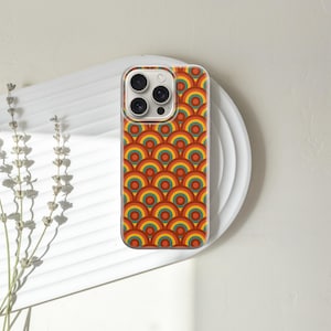 Pode incluir: Capa de telem&oacute;vel com um padr&atilde;o de arco-&iacute;ris retro em tons de laranja, amarelo e verde. A capa est&aacute; sobre um prato branco com um raminho de flores secas. A capa tem uma borda transparente e um recorte para a c&acirc;mara.