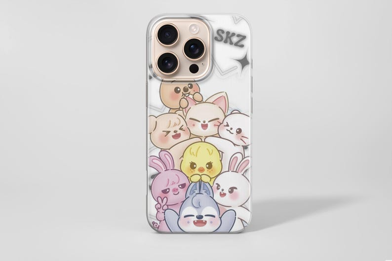 May include: Clear phone case featuring a cartoon illustration of several cute animal characters in various colors. The word "SKZ" is printed in gray at the top. The case is designed to fit a smartphone.