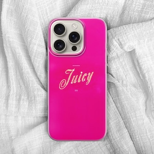 May include: A bright pink phone case with the word "Juicy" in a cursive font. The case has a glossy finish and a camera module with three lenses. The phone case is on a white, textured fabric.