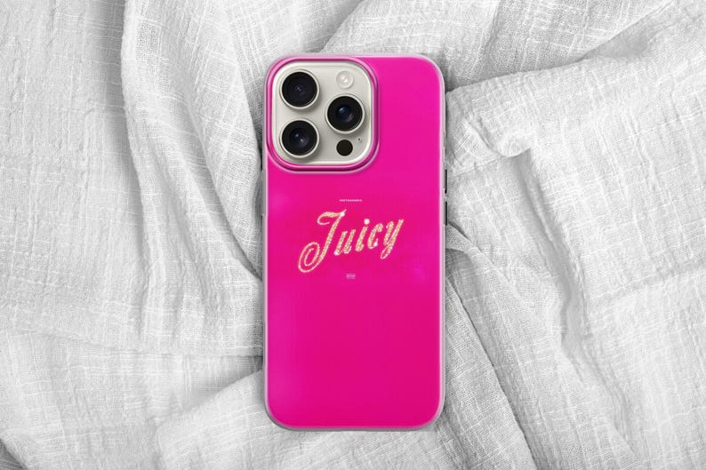 May include: A bright pink phone case with the word "Juicy" in a cursive font. The case has a glossy finish and a camera module with three lenses. The phone case is on a white, textured fabric.