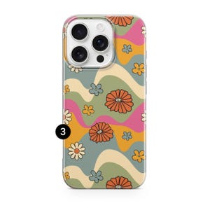 Pode incluir: Uma capa de telefone com um design floral retro colorido. A capa apresenta um padr&atilde;o de flores laranja, rosa e amarelas sobre um fundo ondulado verde, creme e laranja. A capa tem uma borda transparente e um n&uacute;mero 3 preto.