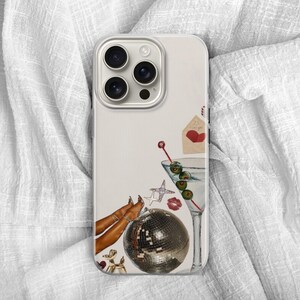 Puede incluir: Una funda de tel&eacute;fono con un fondo crema que presenta una copa de martini con aceitunas, una bola de discoteca, un coraz&oacute;n rojo y una estrella. La funda tiene una lente de c&aacute;mara plateada y un borde de color claro.
