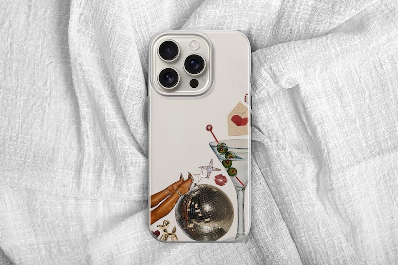 Puede incluir: Una funda de tel&eacute;fono con un fondo crema que presenta una copa de martini con aceitunas, una bola de discoteca, un coraz&oacute;n rojo y una estrella. La funda tiene una lente de c&aacute;mara plateada y un borde de color claro.