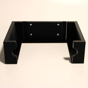May include: A black, rectangular bracket with a recessed center section and rounded cutouts on the sides. The bracket has four pre-drilled holes for mounting. The design is simple and modern, suitable for various applications.