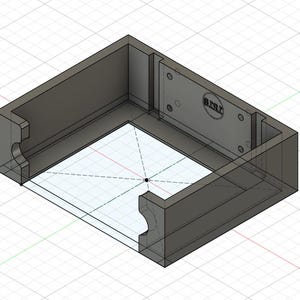 May include: A 3D-rendered, gray rectangular box with a recessed interior and a transparent base. The box features curved cutouts on two sides and a rectangular plate with the text "B.R.E.T." and several small circles.