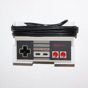 May include: A retro Nintendo controller with a black cable wrapped around it. The controller features a directional pad, start and select buttons, and two red buttons. The word "Nintendo" is printed on the controller.