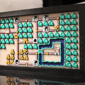 May include: A framed, pixelated map featuring a video game level design. The artwork includes green trees, a blue river, and various character icons. The frame is black, and the overall aesthetic is retro.