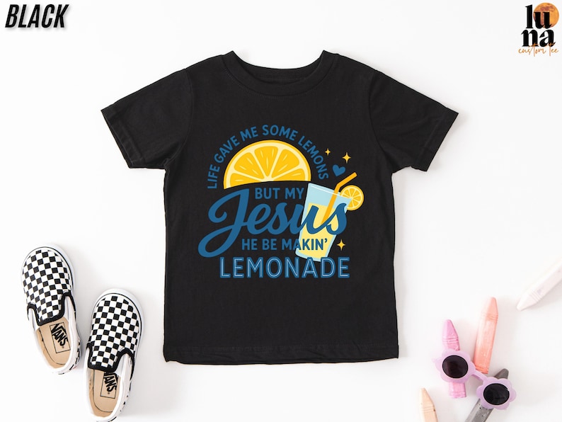 A black t-shirt with a colorful graphic design, including a lemon slice, a drink, and text that says "Life gave me some lemons but my Jesus he be making lemonade".