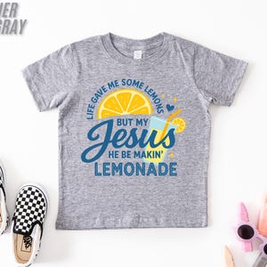 A gray t-shirt with a graphic design, a pair of black and white checkered shoes, and some children's sunglasses on a white background.