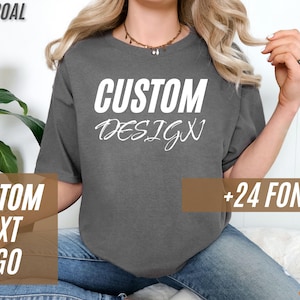 May include: Charcoal-colored t-shirt with the words "CUSTOM DESIGN" in white block letters. The shirt also features the text "CUSTOM TEXT LOGO" and "+24 FONTS" in a brown rectangular box. A logo is in the bottom right corner.
