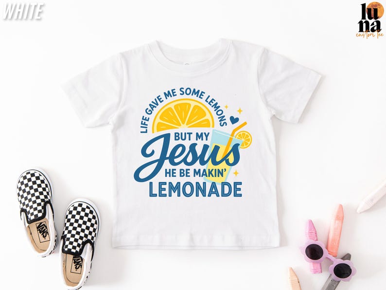 A white t-shirt with a colorful graphic design, including a lemon slice, a cup, and text that says "Life gave me some lemons, but my Jesus he be making lemonade".