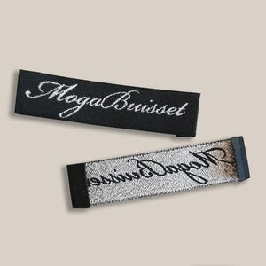 May include: Two rectangular fabric labels. The top label is black with white embroidered text that reads "Moga Buisset". The bottom label is silver with black embroidered text that reads "Moga Buisset".