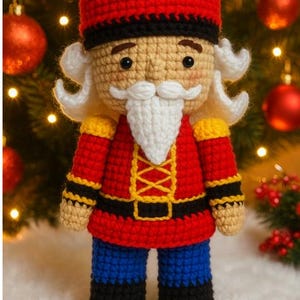 Puede incluir: Muñeco cascanueces de ganchillo. Lleva un gorro y una chaqueta rojos con detalles dorados, pantalones azules y botas negras. Tiene barba y pelo blancos, sobre un fondo de árbol de Navidad con adornos.
