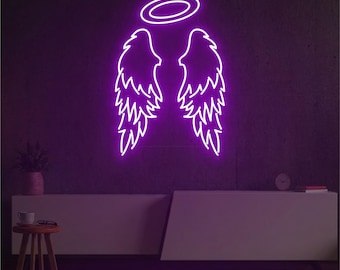 May include: A neon sign in the shape of angel wings and a halo, glowing with a bright purple light against a dark purple wall. The sign is mounted above a white cabinet. A small wooden stool and a plant are in the foreground.
