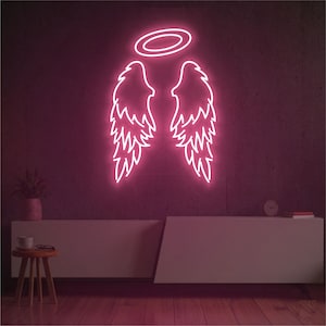 May include: A neon sign depicting angel wings and a halo, glowing in a bright pink hue. The sign is mounted on a dark, textured wall. The room features a white cabinet, a small wooden stool, and a plant.