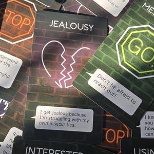 May include: A collection of relationship advice cards with neon-style graphics and text. Cards include phrases like "Message Me," "Jealousy," and "Don't be afraid to reach out!" The cards have a brick wall background.