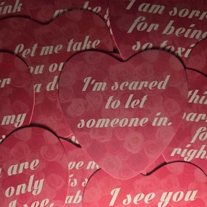 Könnte beinhalten: Eine Sammlung herzförmiger Aufkleber mit einem rosa Rosenmuster-Hintergrund und weißem Text. Sichtbare Sätze sind unter anderem I'm scared to let someone in, I am sorry for being so toxic, let me take you on a date und I see you.