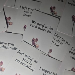 Puede incluir: Una colección de tarjetas rectangulares blancas con texto impreso en negro e ilustraciones pequeñas de rosas rosas secas. Las tarjetas muestran varias frases, incluyendo I can't stop thinking about you, We need to let each other go y I regret lying to you.