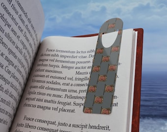 Puede incluir: Un marcapáginas gris con un patrón de banderas de rebanadas de pizza rojas está insertado en un libro abierto. El libro muestra texto impreso. El fondo muestra un cielo azul y el mar.