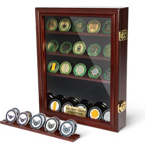 以下が含まれることがあります： ガラス張りのフロントを備えた木製のディスプレイケースで、軍事チャレンジコインを展示しています。ケースは濃い茶色で、複数の棚があります。木製のスタンドには、前景にさらにコインが置かれています。コインにはさまざまなデザインと色があります。