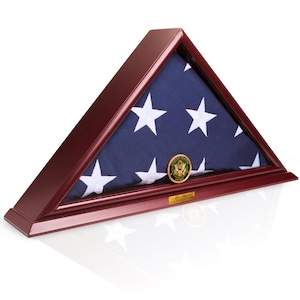 Könnte beinhalten: Eine dreieckige Holz-Fahnenvitrine mit burgunderroter Oberfläche. Im Inneren ist eine gefaltete amerikanische Flagge mit weißen Sternen auf blauem Grund zu sehen. Ein goldfarbenes Army-Emblem ist an der Flagge befestigt. Unten befindet sich eine kleine Tafel mit Text.