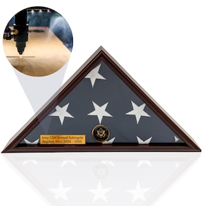 Könnte beinhalten: Eine dunkle Holz-Fahnenvitrine mit Glasfront, die eine gefaltete amerikanische Flagge zeigt. Das Gehäuse hat einen dunkelbraunen Rahmen und eine kleine Plakette mit Text. Ein goldfarbenes Emblem ist auf der Flagge zentriert.