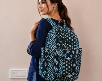May include: A quilted fabric backpack featuring a dark blue and teal color palette with a mix of geometric chevron patterns and small floral motifs. The bag includes a front pocket with a flap closure, side pockets, and adjustable shoulder straps.