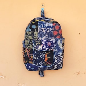 Może przedstawiać: Plecak patchwork z różnymi tkaninami we wzory w kolorze niebieskim, czarnym i czerwonym. Plecak ma małą przednią kieszeń i kieszeń boczną. Wisi na ścianie na niebieskiej pętli.