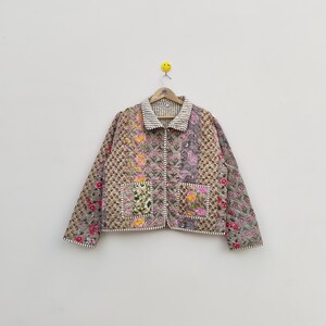 May include: A quilted jacket featuring a patchwork design with various floral and paisley patterns in shades of pink, yellow, brown, and grey. The jacket has a collared neckline, long sleeves, two front pockets, and white striped trim.