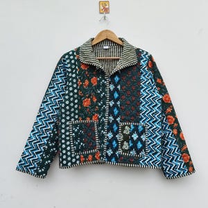 May include: A patchwork jacket with a variety of patterns and colors. The jacket features a mix of floral, geometric, and dotted designs in shades of green, blue, and orange. It has a collared neckline and two front pockets.