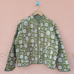 May include: A green quilted jacket with a white floral pattern. The jacket has long sleeves, a button-up front, and two front pockets. The collar and trim feature a striped design. The jacket is hanging on a wooden hanger.