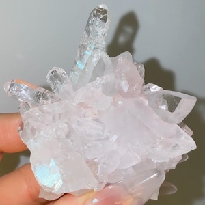 May include: A cluster of translucent, pale pink quartz crystals featuring a prominent, elongated central point. The mineral formation displays sharp, angular facets with subtle iridescent reflections and a clear, glassy texture throughout the structure.