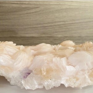 May include: A large, raw mineral specimen featuring clusters of translucent, pale peach and white crystalline formations. The structure displays jagged, layered edges and a glossy, multifaceted surface texture throughout the entire cluster.