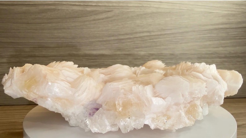 May include: A large, raw mineral specimen featuring clusters of translucent, pale peach and white crystalline formations. The structure displays jagged, layered edges and a glossy, multifaceted surface texture throughout the entire cluster.