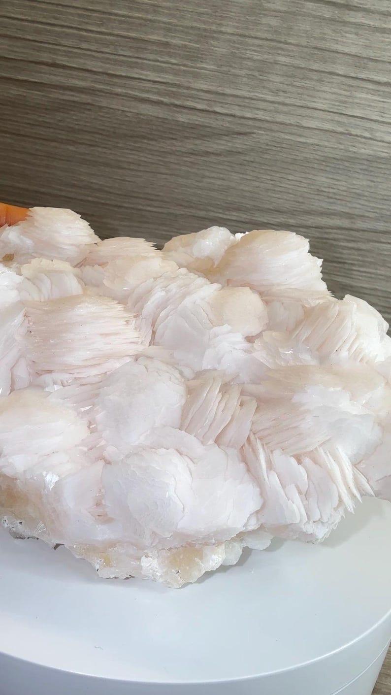 May include: A cluster of pale pink, layered, plate-like mineral crystals forming a dense, textured formation. The specimen features numerous thin, stacked crystalline sheets with a soft, translucent appearance and a light, creamy coloration.